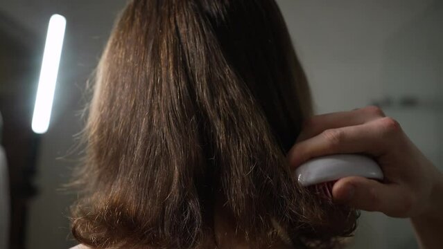 Long-haired man combs his hair with a hairbrush in the bathroom, rear view