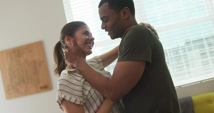 Attractive young millennial couple holding each other and kissing at home. African American and Caucasian man and woman deeply in love . 4k slow motion handheld