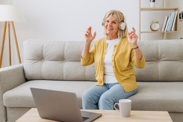 Happy senior woman wearing headphones while listening to music at home