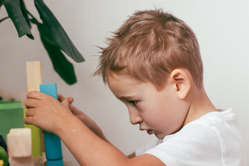 a boy plays with a multi-colored construction set in the form of geometric shapes in a bright room