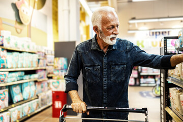 A gray-haired pensioner in a grocery store chooses groceries. Senior customer buying in supermarket.