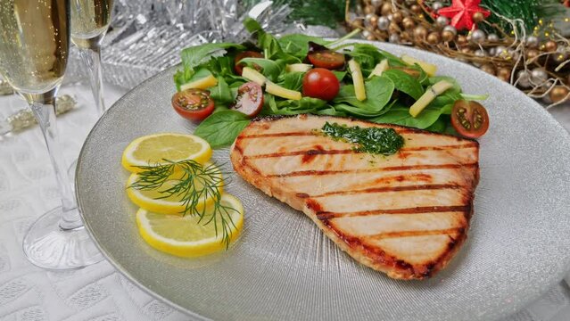 Grilled swordfish steak with fresh salad, tomatoes and cheese on a plate rotating. Christmas New Year decoration. Pour champagne into a glass. Close up