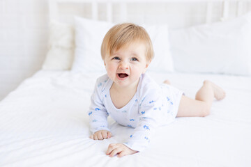 a yawning baby boy of six months blonde wants to sleep on a cot lying on his stomach in a room at home with white cotton bedding, the concept of baby products and accessories or healthy sleep