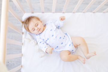 cute sleeping baby boy blonde in a crib house on white cotton bedding, healthy sleep child
