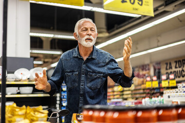 Photo of a mature man feeling surprised about rising food prices in supermarket.