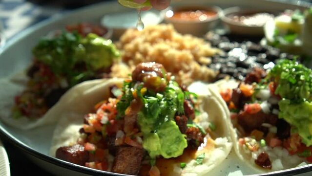 Hand sqeezing lime lemon over soft carnitas avocado taco Mexican salsa food
