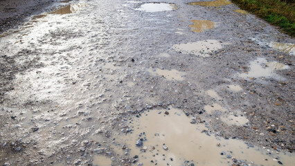 panoramic view of wet dirty gravel road with puddles in village after rain on autumn day - obrazy, fototapety, plakaty
