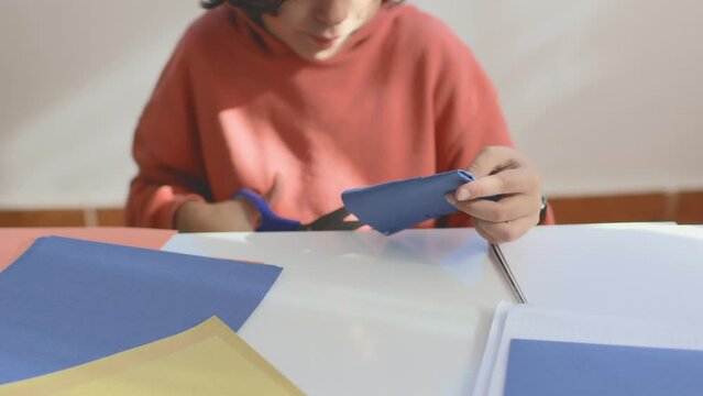 A child cuts out colored paper with scissors. a boy cuts a pattern from blue paper with scissors while sitting at the table. children's creativity.