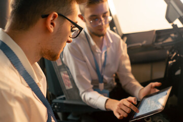 pilots in the cockpit of the plane near the control panel with a tablet in their hands discuss the route before the start of the flight simulator - obrazy, fototapety, plakaty