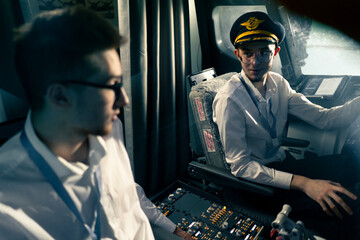 young pilots in the cockpit of the plane control the air transport during the flight the sun shines from the window in the far distance simulator