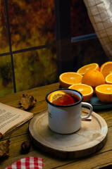 Cup of autumn tea with a book and yellow dry leaves near a window, copy space. Hot drink for autumn cold rainy days. Hygge concept, autumn mood.