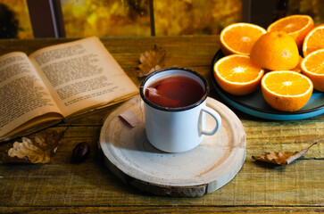 Cup of autumn tea with a book and yellow dry leaves near a window, copy space. Hot drink for autumn cold rainy days. Hygge concept, autumn mood.