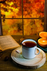 Cup of autumn tea with a book and yellow dry leaves near a window, copy space. Hot drink for autumn cold rainy days. Hygge concept, autumn mood.