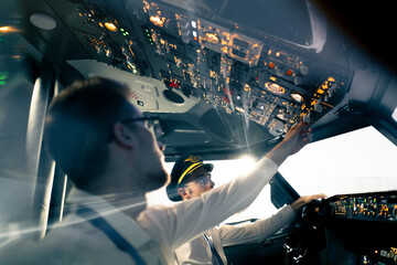 young pilots in the cockpit of the plane control the air transport during the flight the sun shines from the window in the far distance simulator - obrazy, fototapety, plakaty