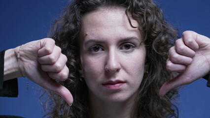 Woman giving thumbs down rejecting offer, close-up face of female person in 20s giving negative...