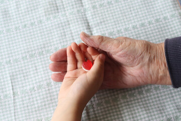 Child hand holding with grandma hand with heart shape gummy sweet. Love caring concept. Red heat...