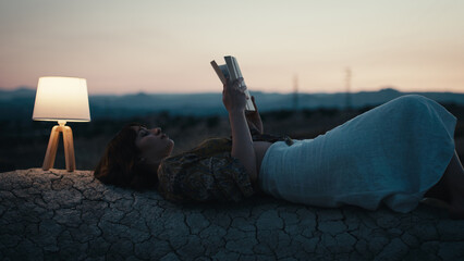 Girl reads a book on a rock with abat jour in the evening