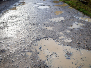 surface of wet dirty gravel road with puddles in village after rain on autumn day