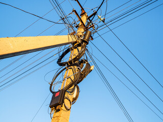 bottom view of concrete power line pole with lot of wires illuminated by sun in village and blue...