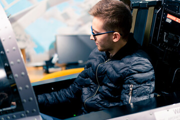 a young guy sits in a flight simulator of a military plane before the start of a virtual flight of...