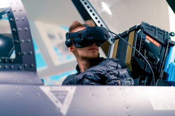 boy sitting in flight simulator of military plane wearing virtual reality glasses during flight...