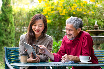 young woman health insurance broker presents insurance benefits to businessman customer by using tablet computer outdoors at coffee shop