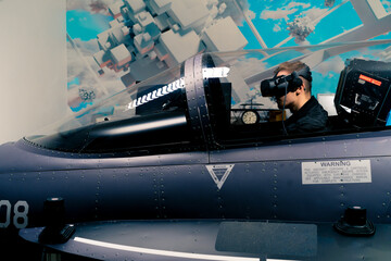 boy sitting in flight simulator of military plane wearing virtual reality glasses during flight...