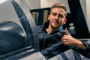 satisfied young guy sitting in flight simulator of military plane after virtual flight shows hand...