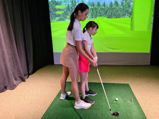 Woman coach teaches a child girl to play golf