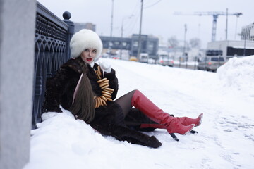 Woman with big braid in brown retro fur coat in winter street with snow. Winter cold weather. Girl...