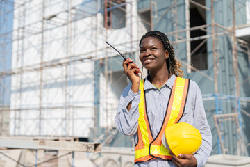 African American engineer woman using radio talking instructing and checking building progress on...