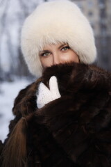 Woman with big braid in brown retro fur coat in winter street with snow. Winter cold weather. Girl...