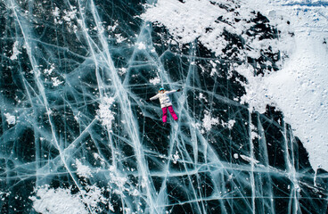 Aerial top down shot of the young woman lying on the blue cracked ice of Baikal and shaking hands...
