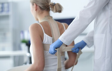 Doctor putting corset on back of female patient closeup. Spinal curvature treatment concept