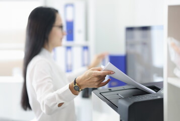 Young woman pulling paper out of printer closeup. Replacement of cartridges and repair of office...