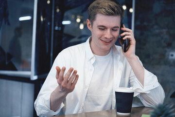 Smiling male coworker talking on the smartphone at her workplace in the office. Coffee on the table. Startup, strategy, business concept