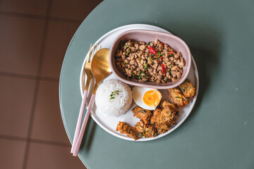 Stir fried Thai basil with minced pork and chili side with rice, boiled egg, and fired vegetable on green table. Thai local food style.