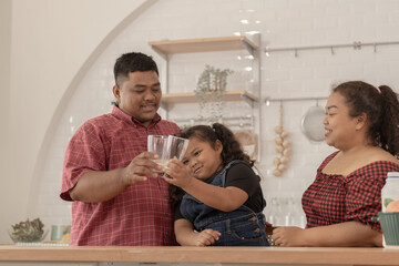 A chubby family with a father wearing a prosthetic. They were happily inviting their girl to drink morning milk together in the kitchen of their home. Breakfast time of Asian dad mom and kid people.