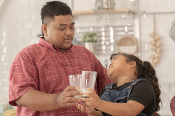 A chubby family with a father wearing a prosthetic. They were happily inviting their girl to drink morning milk together in the kitchen of their home. Breakfast time of Asian dad mom and kid people.