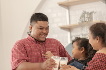 A chubby family with a father wearing a prosthetic. They were happily inviting their girl to drink morning milk together in the kitchen of their home. Breakfast time of Asian dad mom and kid people.