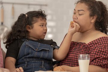 close up face of a Cute Asian girl eating a snack with family. Pretty Black Child Eating Snack At Home. Preschool Kid Having A Bite With Fresh Baked Biscuits.