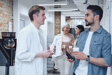 Smiling two men talking while standing at the office with cups of coffee. Teamwork, startup, business concept