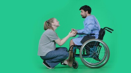 Adult man patient in robe sitting in wheelchair girl next to him on knees holding his hand, supporting expression. Isolated on chroma key green screen.