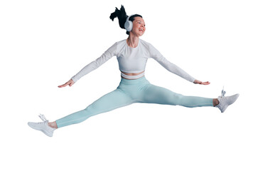 Excited young woman in sportswear jumping high against transparent background listening motivative music using headphones looks away toothy smiling. Sport club.