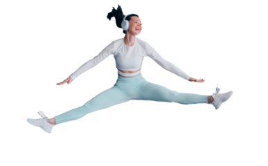 Excited young woman in sportswear jumping high against transparent background listening motivative music using headphones looks away toothy smiling. Sport club.