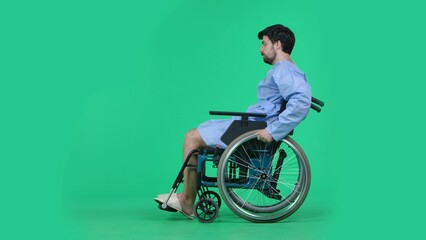 Adult man patient in robe sitting in wheelchair and riding on it helping to spin the wheels with hands. Isolated on chroma key green screen..