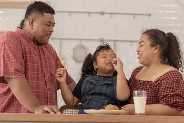 Cute Asian girl eating a snack with family. Asian family having breakfast together at pantry...