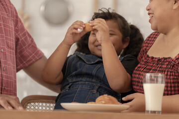 close up face of a Cute Asian girl eating a snack with family. Pretty Black Child Eating Snack At Home. Preschool Kid Having A Bite With Fresh Baked Biscuits.