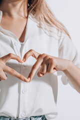 romantic young woman in shirt making a heart gesture with her fingers in front of her chest showing...