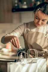 Happy woman bakery shop owner pours confetti into a bag for customer order. Bakery chef baking pastry and cake in kitchen. Small business entrepreneur and food delivery concept.